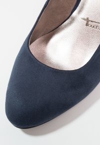 Gros plan sur une chaussure plate pour femme en daim bleu marine avec un bout arrondi et une semelle intérieure argentée métallique.