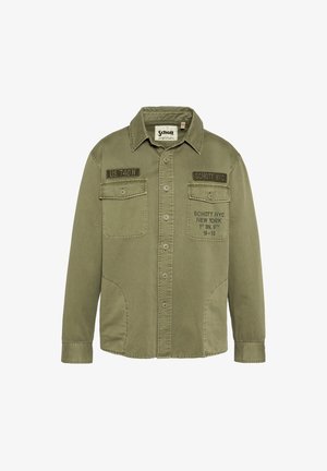 Olivengrøn knap-op bomuldsjakke med to brystlommer, trykt tekst "Schott NYC New York 1st BN. 9th 19-13" på højre lomme.