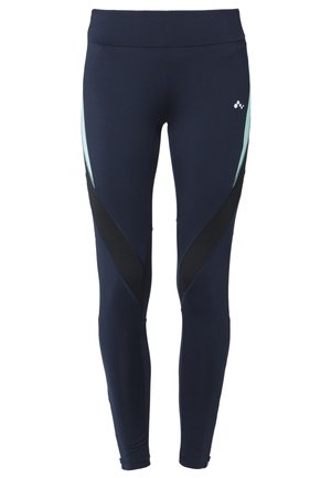 Kvinde, der går, iført hvid t-shirt, mørkeblå leggings med lyseblå og sorte diagonale paneler og hvide løbesko på en ensfarvet baggrund.