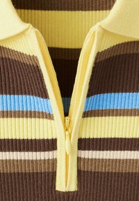 Haut en maille côtelée rayé jaune, marron, bleu et beige avec une fermeture éclair jaune partiellement ouverte et un col pointu.