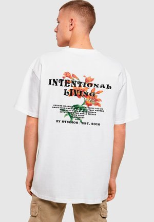 Hvid bomulds t-shirt med et blomsterdesign og teksten "INTENTIONAL LIVING" i fed sort skrift på ryggen.
