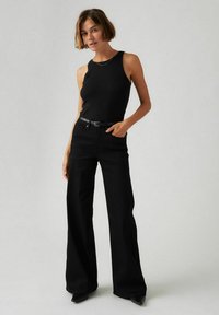 Un haut noir à côtes sans manches associé à un jean noir à jambes larges, avec une ceinture noire et des chaussures noires à talons fins. Design simple et minimal.