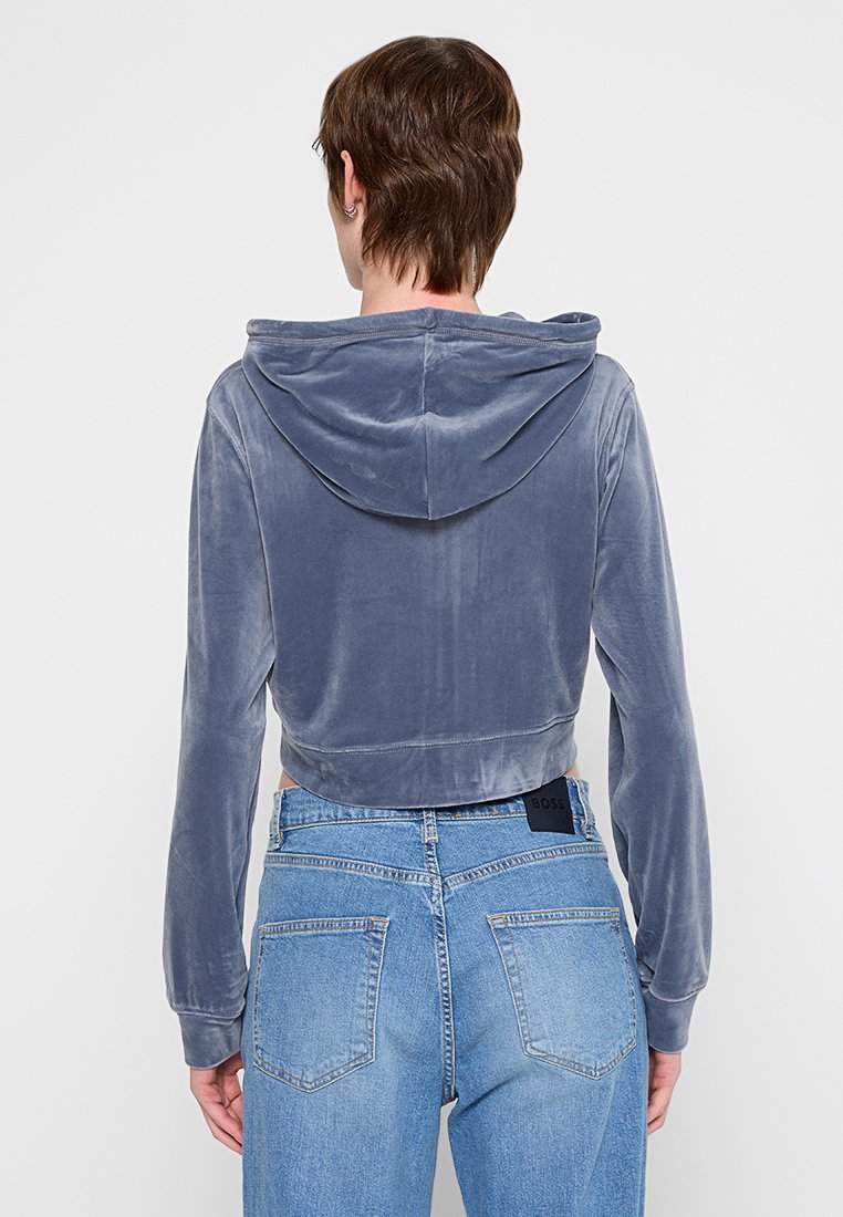 Geknipt hoodie van zacht, blauw fluweel met een trekkoordkap. Beschikt over lange mouwen en een gladde, textuurafwerking. Gemaakt in combinatie met high-waisted jeans.