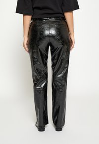 Melna, spīdīga mākslīgās ādas bikses ar taisnu kājas dizainu, centrālu aizmugures šuvi un atvērtām kabatām aizmugurē. Gluda tekstūra un augsta spīduma apdare.