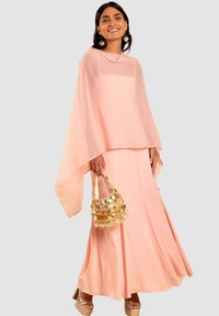 Rosa fließendes Kleid mit einer kapellenartigen Überlage und taillierter Taille, kombiniert mit einer schimmernden goldenen Tasche und beigen Riemchen-Heels.