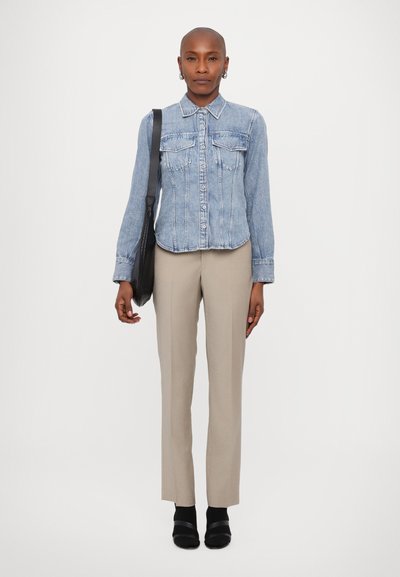 Denim button-up skjorte med to brystlommer, kombinert med beige tilpassede bukser og svarte sko. Enkelt design med klassisk passform.