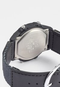 Relógio de borracha preta com fundo em aço inoxidável, apresentando dois botões redondos prateados, pulseira em couro e um design texturizado e trançado na fita.