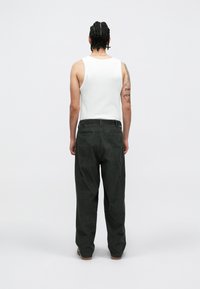 Balta maikė be rankovių ir tamsiai žalia velveto kelnės, tiesaus kirpimo su tekstūruotu paviršiumi ir galiniais kišeniais, matomos iš nugaros.