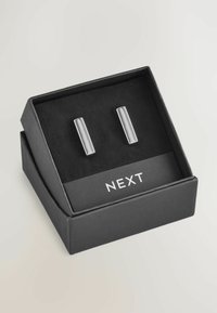 Silberfarbene Manschettenknöpfe, präsentiert in einer schwarzen Box mit einem weichen Innenfutter; rechteckiges Design mit polierter Oberfläche und dezentem Gravur.