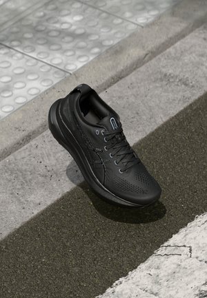 Zwarte sportieve sneaker met veters die op een getextureerd trottoir ligt, dichtbij een stoeprand en voelbare tegelstrook voor slechtziende voetgangers.