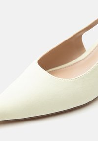 Κρεμ χρωματιστό, μυτερό γυναικείο παπούτσι slingback με επίπεδη σόλα, με λείο υλικό και ανοιχτό μπεζ εσωτερική επένδυση σε λευκό φόντο.