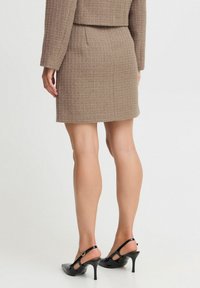Bruine, gestructureerde minirok met een aansluitend ontwerp. Gekomplementeerd met zwarte, hoge hakken met een slingback en een spitse neus en enkelbandje.