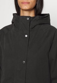 Black hooded jacket made of a textured fabric, featuring snap buttons and side pockets, with a clean, modern design.