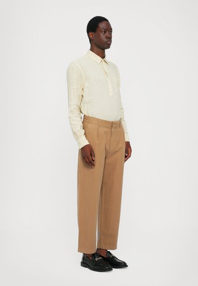 Lys beige langermet skjorte med knapp Collar, kombinert med høytrukne beige bukser og svarte loafers. Enkelt design og passform.
