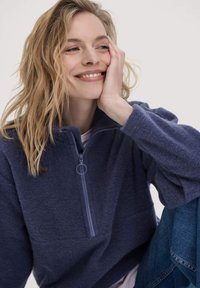 Marineblauer Fleece-Pullover mit hohem Kragen, halbem Reißverschluss und strukturiertem Stoff. Verfügt über eine lockere Passform und eine Fronttasche.