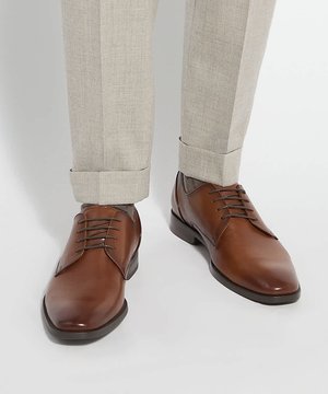 Braune Leder-Schnür-Dressschuhe, getragen zu hellbeigen, umgekrempelten Hosen vor weißem Hintergrund.