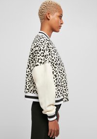 Jakna bomber s leopard uzorkom na krem osnovi, s kontrastnim bijelim rukavima, prugastim manžetama i opuštenim krojem. Mekani teksturirani materijal.