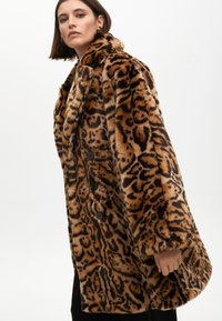 Kaput s umjetnim krznom s leopard uzorkom, slobodnog kroja, širokim ovratnikom i crnim gumbima, s mekanom teksturom u smeškim i crnim tonovima.