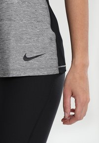 Maglietta sportiva grigia con tessuto a trapuntatura, dettagli neri e un piccolo logo Nike nero. Abbinata a leggings neri lisci.