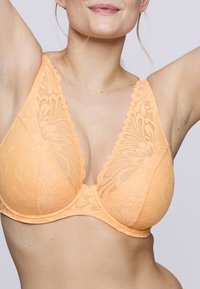 Sostén de encaje melocotón con copas triangulares, que presenta patrones florales, bordes festoneados y tirantes ajustables. Textura suave, soporte con aros.