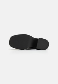 Sole di scarpa nera con superficie testurizzata, punta arrotondata e tacco leggero. Design piatto con bordi lisci e senza marchi visibili.