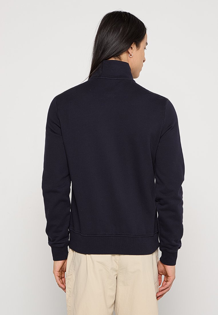 Mörkblå sweatshirt med hög krage, ribbade ärmslut och en strukturerad textil. Har en enkel design utan synliga logotyper eller mönster.
