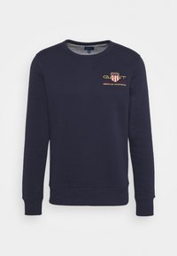 Sudadera azul marino de algodón, con cuello redondo y mangas largas. Incluye un logo bordado en rojo, amarillo y blanco.