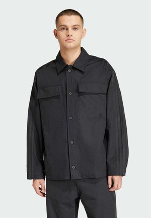 Zwarte button-up jas met twee voorzakken, voorzien van een ribbelstructuur en subtiele strepen langs de schouders. Wasmachinebestendige stof.
