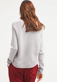 Lichtgrijs langslijf top met horizontale ribbelstructuur, afgeronde zoom, gecombineerd met bordeauxrode broek. Eenvoudig ontwerp, casual pasvorm.