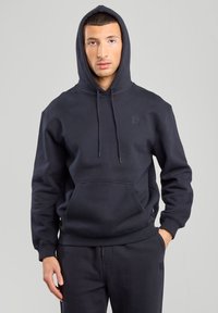 Felpa nera con cappuccio, tasca frontale e coulisse, realizzata in tessuto morbido. Presenta un piccolo logo del marchio sulla parte alta del petto.