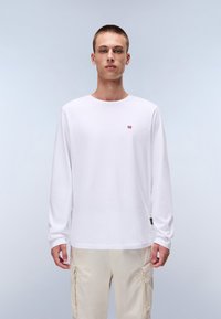 Langærmet hvid t-shirt lavet af bomuld, med et lille logo på brystet. Enkel, rund halsudskæring og afslappet pasform.