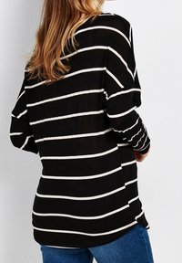 Czarna i biała bluzka z długim rękawem, o luźnym kroju i szczelinach po bokach dla swobody ruchów. Miękki, lekki materiał.