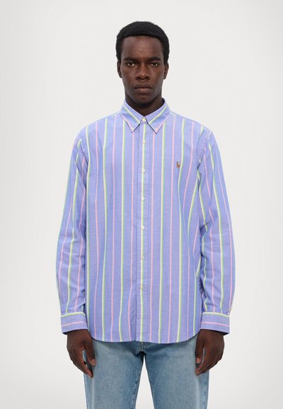 Chemise à manches longues à boutons de couleur lilas clair avec des rayures verticales rose, vert et bleu. Elle est dotée d'un col et d'un petit logo sur la poitrine.