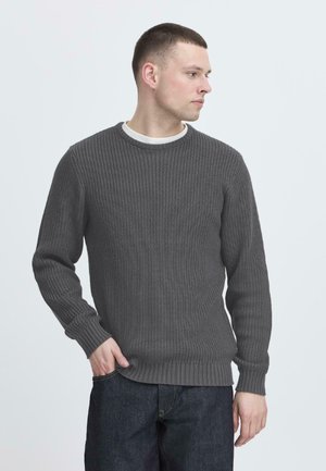 Grå ribbestrikket genser med rund hals, med lange ermer og teksturert strikk. Kombinert med mørk denimjeans.