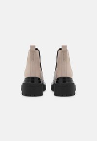 Botines negros y beige con suela gruesa, textura suave, paneles laterales elásticos y tiradores en la parte trasera.