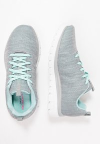 Baskets de sport grises avec une tige en maille respirante, des lacets bleu clair et une semelle blanche rembourrée. Elles possèdent une languette à l'arrière.