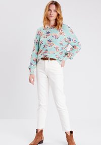 Maglione turchese con motivo floreale, maniche lunghe, vestibilità comoda. Abbinato a pantaloni bianchi e stivaletti marroni. Tessuto morbido.