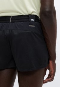 Μαύρο αθλητικό σορτς με υφή, ελαστική μέση και μικρή ετικέτα λογότυπου στο πίσω μέρος. Το σορτς είναι εφαρμοστό και πάνω από το γόνατο.