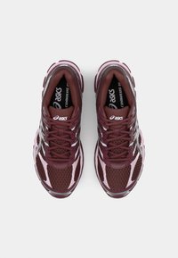 Burgundske tekaške čevlje z mrežastim materialom, reflektivnimi detajli in roza podrobnostmi. Imajo sistem vezalk in podplate s blaženjem za udobje.