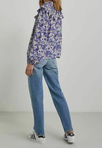 Blommig blus med volangkrage i lila och vitt, kombinerad med ljusblå raka jeans och svartvita sneakers.