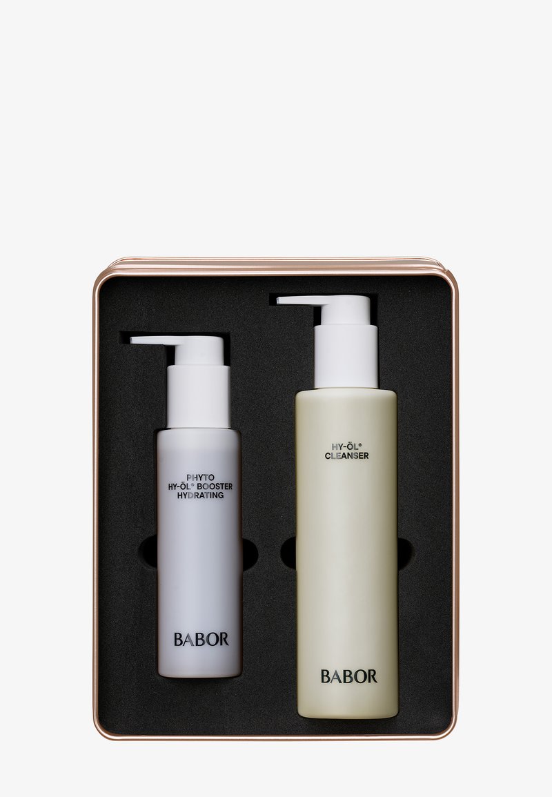 Ensemble de deux produits de soins dans une boîte en métal avec un couvercle en or rose. Comprend une bouteille blanche à pompe et une bouteille verte à pompe, toutes deux étiquetées.