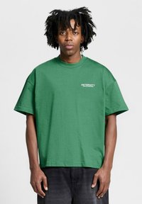 Camiseta de algodón verde con mangas cortas, corte holgado y cuello redondo. Presenta el texto blanco "ETERNITY" en el lado izquierdo del pecho.