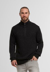 Schwarzer Strickpullover mit hohem Kragen und halbem Reißverschluss, ausgestattet mit einem strukturierten Muster mit weißen Sprenkeln. Rippbündchen und Saum.