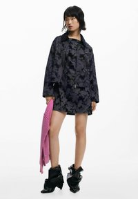 Jachetă cu imprimeu floral negru peste o rochie asortată, cu un șal tricotat roz. Prezentă încălțări cu tocuri ascuțite, negre, și o siluetă relaxată.