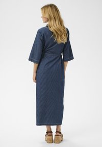 Vestido de rayas náuticas con mangas anchas, cinturón de lazo y corte largo y recto. Sandalias con plataforma de corcho complementan el conjunto.