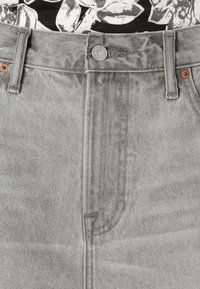 Grå denimjeans med høj talje, der har kobberfarvet hardware, knaplukning og synlige syninger. Teksturen ser slidt ud.