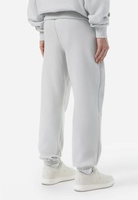 Pantalones de chándal gris claro hechos de material suave, con puños elásticos y un ajuste relajado. Combinados con zapatillas blancas con un logo.