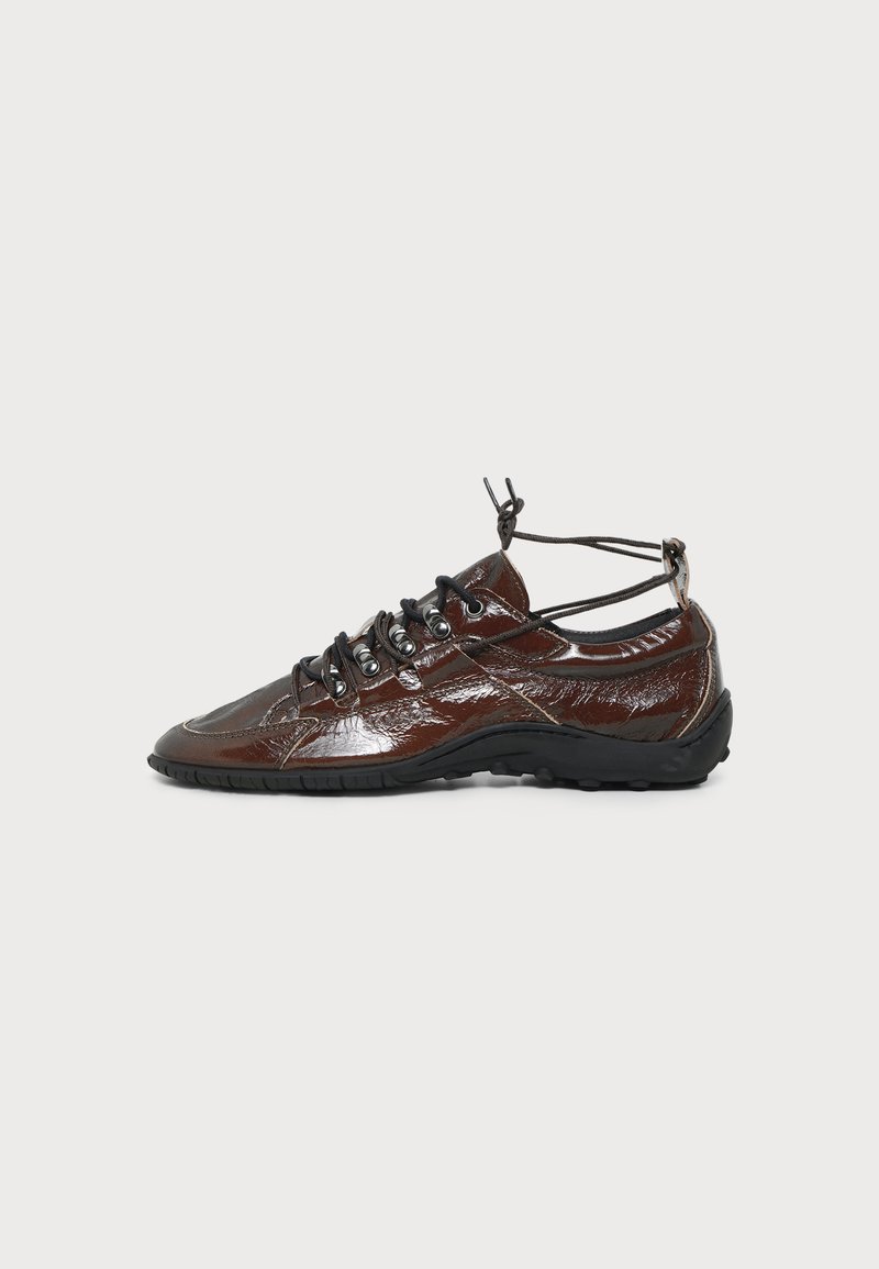 Basket en cuir brillant marron foncé avec semelle noire, laçage noir à l'avant et sangles réglables à la cheville sur fond blanc.