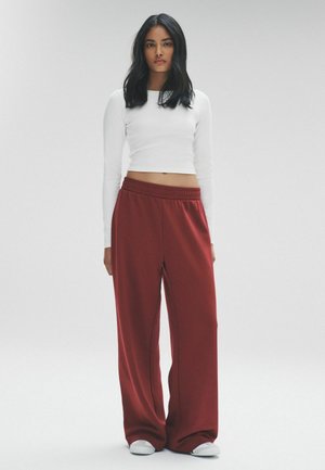 Weißes langärmliges Cropped Top, kombiniert mit lockeren, hoch taillierten bordeauxfarbenen Hosen. Der Stoff wirkt weich, mit einem elastischen Bund und sanften Drapierungen.