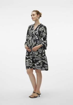 Abito da maternità floreale in bianco e nero con vita legata, maniche lunghe e gonna svasata. Abbinato a tacchi neri con cinturini.